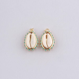 May include: Two gold-colored seashell pendants with a white shell center and a turquoise border. The pendants are oval-shaped and have a small loop at the top for hanging. The background is plain white.