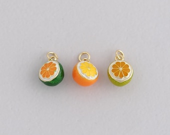 May include: Three colorful fruit charms. One is green with an orange slice, another is orange with a yellow slice, and the last is lime green with an orange slice. Each charm has a gold-colored loop at the top for attaching to jewelry.