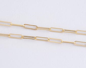 May include: Close-up of two gold-colored paperclip chain necklaces. The chains are made of rectangular links connected by small, thin bars. The background is a plain white surface, highlighting the jewelry's design and color.