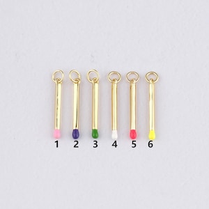 Op de afbeelding: Zes goudkleurige lucifersbedels met gekleurde uiteinden. De uiteinden zijn roze, paars, groen, wit, rood en geel. Elke bedel heeft een kleine lus aan de bovenkant om aan sieraden of andere knutselwerken te bevestigen. De nummers 1 tot en met 6 staan eronder.