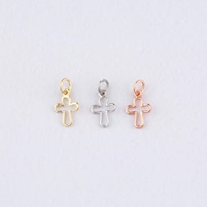 Op de afbeelding: Drie kleine kruisbedels in goud, zilver en roségoud. Elke bedel heeft een lusje voor eenvoudige bevestiging aan sieraden. De kruizen zijn open-werk, met een eenvoudig, elegant ontwerp. De achtergrond is licht van kleur.