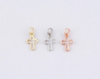 May include: Three small cross charms in gold, silver, and rose gold. Each charm has a looped top for easy attachment to jewelry. The crosses are open-work, with a simple, elegant design. The background is a plain, light color.