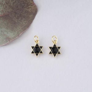 May include: Two gold-toned charms in the shape of a six-pointed star, also known as the Star of David. The stars are black enamel with a gold outline.