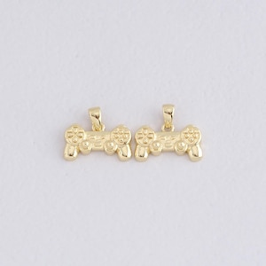 May include: Two gold-colored pendant charms shaped like video game controllers. Each charm has a loop at the top for attaching to a chain or bracelet. The controllers feature buttons and directional pads.