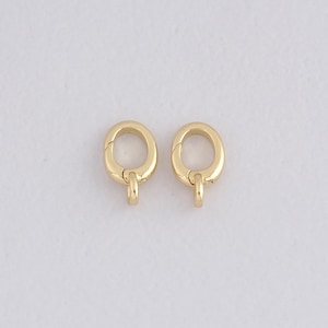 May include: Two gold-colored oval-shaped clasps with a small loop at the bottom. The clasps are shown against a white background. These clasps are likely used for jewelry making or other craft projects.