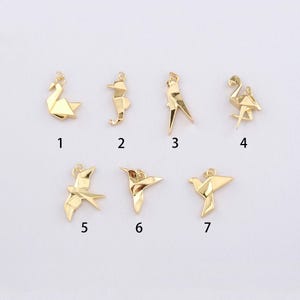 K&ouml;nnte beinhalten: Eine Sammlung von sieben goldfarbenen Origami-Anh&auml;ngern in verschiedenen Vogel- und Tierformen. Die Anh&auml;nger zeigen einen Schwan, ein Seepferdchen, einen Vogel, einen Flamingo und einen Kolibri. Jeder Anh&auml;nger ist nummeriert.
