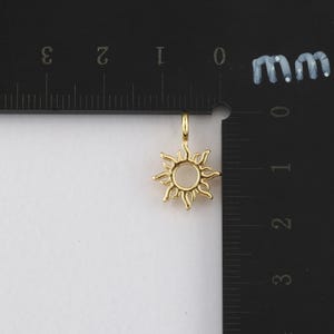 May include: Gold-toned sun charm pendant with a circular center and detailed rays. The charm is measured against a ruler, showing it is approximately 1 cm in diameter.