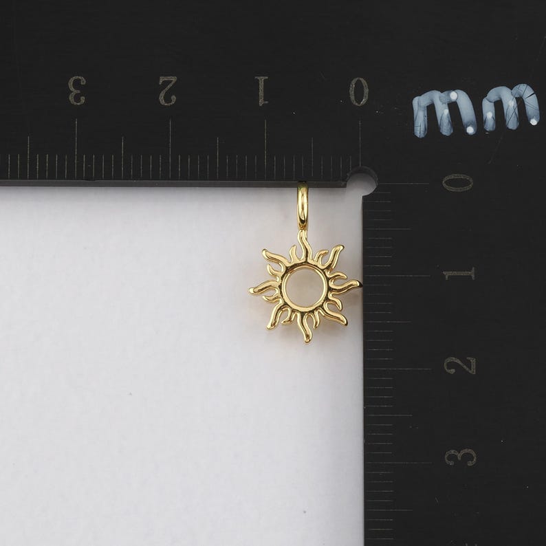 May include: Gold-toned sun charm pendant with a circular center and detailed rays. The charm is measured against a ruler, showing it is approximately 1 cm in diameter.