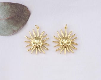 May include: Two gold-toned sun charm pendants with a face on each. The sun has a circular face with a smiling mouth and two eyes. The sun has 12 rays extending from the face.