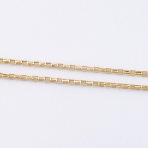 May include: Close-up of a gold-colored chain necklace with a rectangular link design. The chain is displayed against a white background, highlighting its shiny, metallic appearance. The necklace is a simple, elegant piece of jewelry.