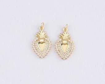 May include: Two gold-colored heart-shaped pendants with a halo of small, clear crystals. Each pendant has a heart in the center and a decorative top. The pendants are on a white background.