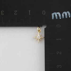 Op de afbeelding: Een gouden stervormige hanger met een heldere strasssteen in het midden. De hanger is ongeveer 1 cm groot.