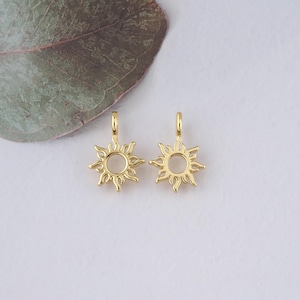 May include: Two gold-toned sun charm pendants with a circular center and a detailed sunburst design. The charms have a loop at the top for attaching to jewelry.
