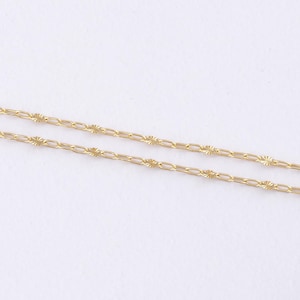 May include: Close-up of two delicate gold necklaces. Each necklace features a chain with small, rectangular links interspersed with starburst-shaped accents. The necklaces are displayed against a plain white background, highlighting their intricate design.