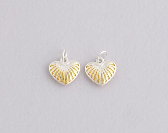 May include: Two silver heart-shaped pendants with gold sunburst patterns. Each pendant has a small loop at the top for attaching to a chain or bracelet. The pendants are set against a light grey background.