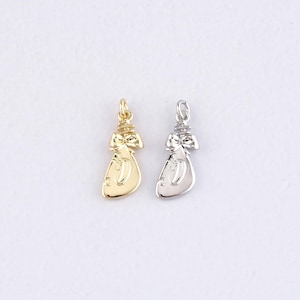 Puede incluir: Dos pequeños colgantes metálicos con forma de bolsa de dinero. Uno es dorado, el otro plateado. Cada colgante tiene un lazo en la parte superior para sujetarlo a un collar o pulsera. Los colgantes están sobre un fondo blanco.