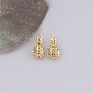 Peut inclure: Deux breloques en forme de larme dorées avec des accents de cristal transparent. Les breloques ont un design délicat et complexe et sont parfaites pour ajouter une touche d'éclat à vos projets de bijoux.