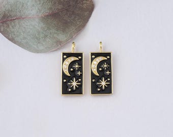 May include: Two gold-toned pendant charms with black enamel and clear rhinestone accents. Each charm features a crescent moon and a star on a black background.