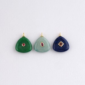 Pode incluir: Três pingentes de pedras preciosas em verde, verde-azulado e azul marinho. Cada pingente triangular tem uma fiança dourada e um pequeno detalhe de pedra preciosa vermelha. O pingente verde tem um detalhe redondo, o verde-azulado tem um oval e o azul marinho tem um quadrado.