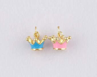 May include: Two small, gold-colored crown charms. One crown has a blue base, and the other has a pink base. Both crowns have a loop at the top for attaching to jewelry. The crowns are set against a plain white background.