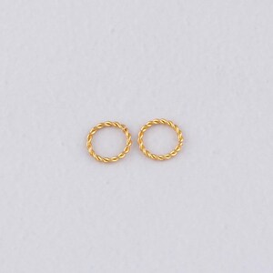 May include: Two gold-colored, twisted-rope style hoop earrings. The earrings are small, circular, and have a textured appearance. They are displayed on a plain white background, highlighting their simple design.