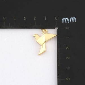 K&ouml;nnte beinhalten: Ein goldfarbener Origami-Vogel-Anh&auml;nger. Der Anh&auml;nger ist eine geometrische Darstellung eines Vogels mit gefalteten Fl&uuml;geln und einer kleinen Schlaufe oben f&uuml;r eine Kette. Der Anh&auml;nger ist etwa 2.5 cm lang.
