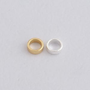 Op de afbeelding: Twee metalen spacer kralen. Eén is goudkleurig, de andere is zilverkleurig. Beide kralen zijn cilindrisch met een gat in het midden. Deze kralen worden gebruikt bij het maken van sieraden.