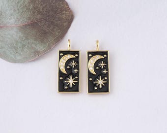 May include: A pair of gold-tone earrings with black enamel rectangular charms. Each charm features a crescent moon, a star, and smaller stars, all set with clear cubic zirconia stones.