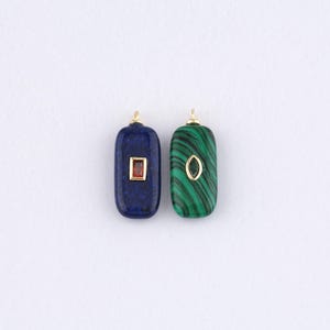 May include: Two rectangular gemstone pendants. One is a deep blue with a small red square, the other is green with black veining and a gold oval. Both have gold-coloured loops at the top for hanging.