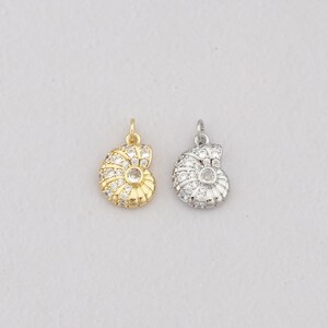 May include: Two nautilus shell charms, one in gold-tone metal and one in silver-tone metal. Each charm features a spiral design encrusted with small, clear, round-cut cubic zirconia stones and a single larger stone at the center of the spiral.