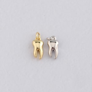 May include: Two tooth-shaped charms. One is gold-colored, the other is silver-colored. Both charms have a loop at the top for attaching to a necklace or bracelet. The charms are likely made of metal and are designed to resemble a molar.