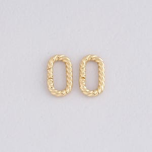 May include: Two gold-colored oval-shaped clasps with a twisted rope design. The clasps are shown against a white background. The clasps are likely for jewelry making or other craft projects.