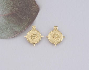 May include: Two gold-toned pendant charms with a circular design featuring a raised sunburst pattern and a beaded border. Each charm has a small loop at the top for attaching to a necklace or bracelet.