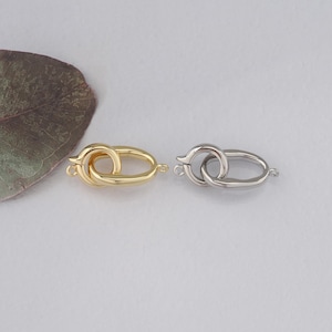 May include: Two metal clasps, one gold and one silver, with a looped design. The clasps are oval shaped and have a smooth finish.