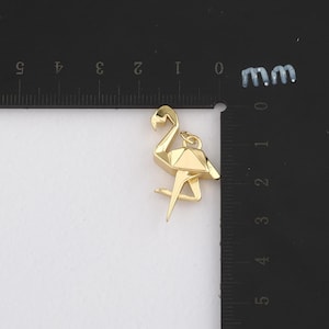 K&ouml;nnte beinhalten: Ein goldfarbener Flamingo-Anh&auml;nger mit geometrischem Design. Der Anh&auml;nger ist etwa 2,5 cm hoch und hat eine Schlaufe zum Befestigen an einer Kette oder einem Armband. Der Flamingo steht auf einem Bein.