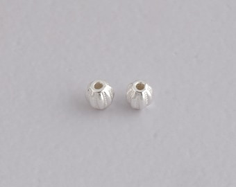 May include: Two small, silver-colored beads with a ribbed, pumpkin-like design. Each bead has a central hole and a slightly textured surface. The beads are displayed against a plain, light gray background, suitable for jewelry making.