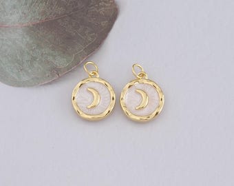 May include: Two gold-colored round pendants with a white enamel background and a gold crescent moon design. The pendants have a textured border and a small loop at the top for attaching to a chain or earring hook. Jewelry.