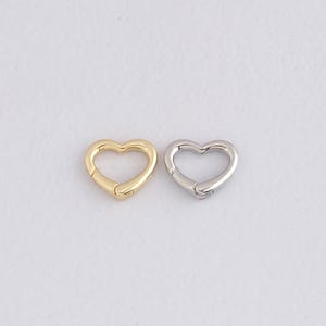 May include: Two heart-shaped clasps, one gold-toned and one silver-toned, are displayed against a white background. The clasps are open, showcasing their functionality. These clasps are ideal for jewelry making or crafting projects.