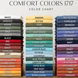 May include: A color chart for Comfort Colors 1717 t-shirts, featuring three vertical stacks of folded fabric in various shades. Each stack includes labels for colors like White, Graphite, Banana, Butter, Mystic Blue, and China Blue, organized by hue.