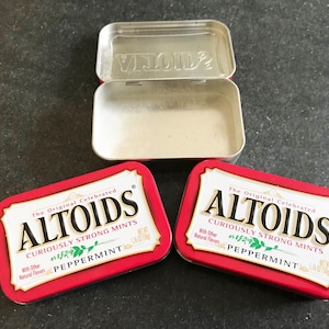 May include: Two red and white Altoids Peppermint mint tins with an open tin. The tins have the text "ALTOIDS CURIOUSLY STRONG MINTS PEPPERMINT" on the front. The open tin is silver.