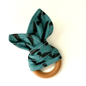 May include: Teal fabric baby teether with a black and white duck print tied around a wooden ring.