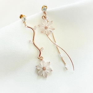May include: A pair of gold earrings with delicate floral designs. Each earring features a white flower with a crystal centre and a dangling chain with small pearls.