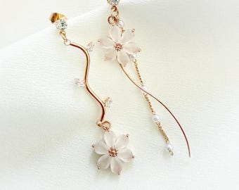 May include: A pair of gold earrings with delicate floral designs. Each earring features a white flower with a crystal center and a dangling chain with small pearls.