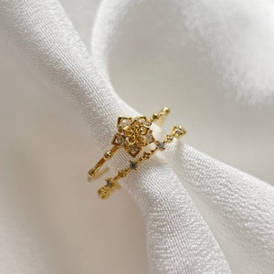 May include: A gold ring set with a delicate floral design and sparkling clear stones. The ring is made of two bands, one with a flower design and the other with a row of stones.