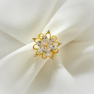 May include: A gold ring featuring a large, clear, flower-shaped design. The ring is set with numerous small, clear stones.