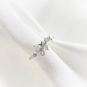 May include: A silver ring with a delicate floral design featuring pastel blue, green, and white gemstones.