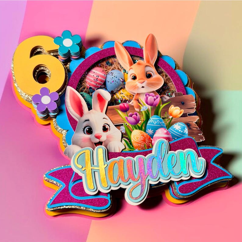 May include: A colorful Easter-themed cake topper featuring two cartoon bunnies, Easter eggs, and flowers. The topper includes the number 6 and the name "Hayden" in a decorative font. The design incorporates shades of pink, blue, yellow, and purple.