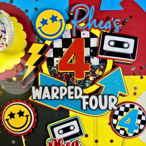 May include: A colorful birthday cake topper with the text "Rhea's" and "Warped Four". The design includes a red number 4, a cassette tape, a smiley face, and a lightning bolt. The background is yellow, red, and blue.