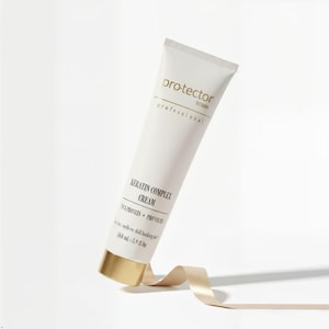 May include: A white tube of "pro-tector professional" keratin complex cream. The tube has gold accents on the cap and text. The cream is 3.9 fl oz (110 ml). A beige ribbon is draped near the bottom of the tube.