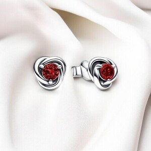 Puede incluir: Un par de pendientes de plata con una piedra preciosa roja en el centro de cada pendiente. Los pendientes tienen forma de nudo.